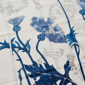 Puede incluir: Una tela blanca con un estampado bot&aacute;nico de acianos en varios tonos de azul. El dise&ntilde;o incluye ilustraciones detalladas de cabezas de flores, capullos y hojas serradas, con algunos elementos en azul s&oacute;lido y otros representados en contorno.