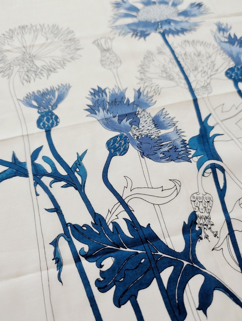Puede incluir: Una tela blanca con un estampado bot&aacute;nico de acianos en varios tonos de azul. El dise&ntilde;o incluye ilustraciones detalladas de cabezas de flores, capullos y hojas serradas, con algunos elementos en azul s&oacute;lido y otros representados en contorno.