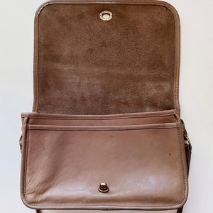 May include: A brown leather shoulder bag with a flap closure and a long strap. The bag is open and the inside is lined with brown suede.