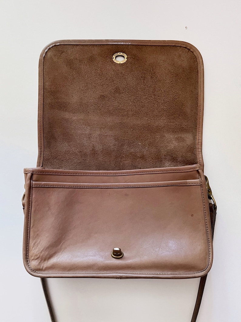 May include: A brown leather shoulder bag with a flap closure and a long strap. The bag is open and the inside is lined with brown suede.