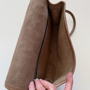 May include: The inside of a brown leather bag with a zipper closure. The bag is lined with a soft, brown fabric.