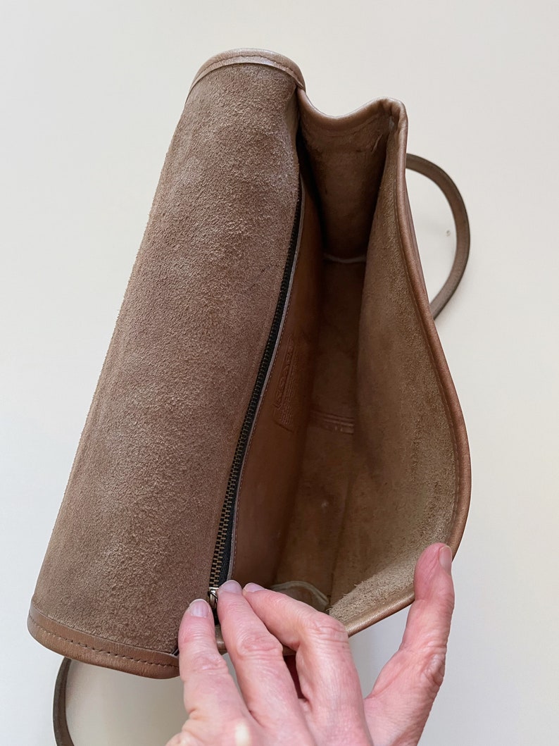 May include: The inside of a brown leather bag with a zipper closure. The bag is lined with a soft, brown fabric.