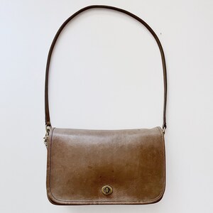 May include: A brown leather shoulder bag with a single strap and a brass clasp.