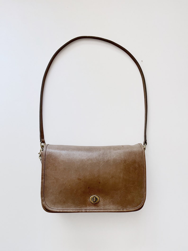 May include: A brown leather shoulder bag with a single strap and a brass clasp.