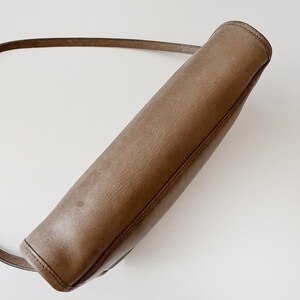 May include: A brown leather shoulder bag with a long strap. The bag is closed and the strap is hanging over the top.