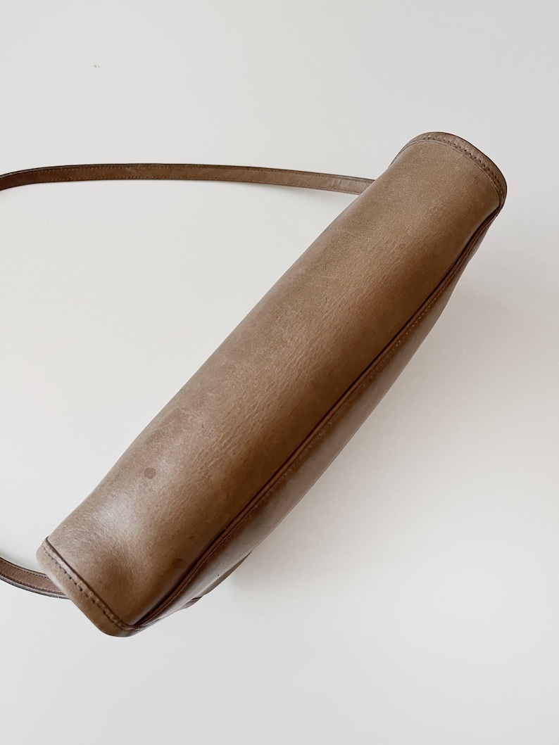 May include: A brown leather shoulder bag with a long strap. The bag is closed and the strap is hanging over the top.