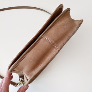 May include: A brown leather shoulder bag with a gold clasp. The bag is closed and the strap is hanging off the bag.