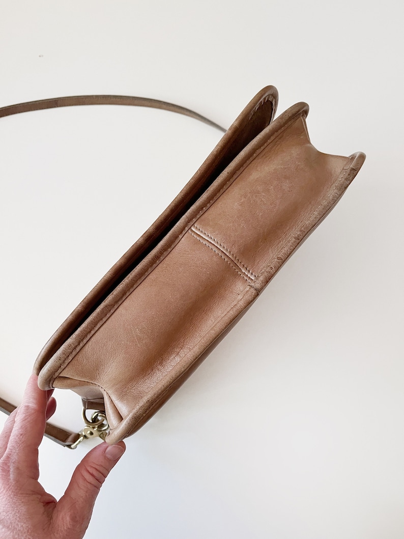 May include: A brown leather shoulder bag with a gold clasp. The bag is closed and the strap is hanging off the bag.