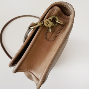 May include: A light brown leather shoulder bag with a brass clasp and a long strap.
