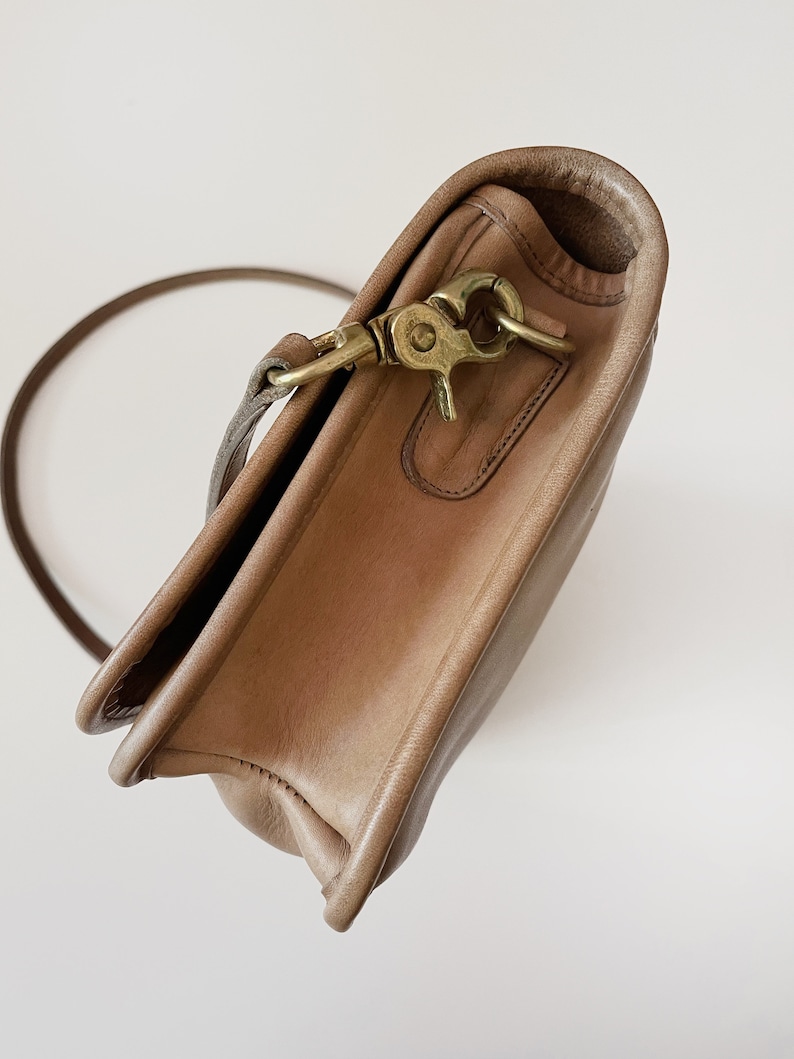 May include: A light brown leather shoulder bag with a brass clasp and a long strap.