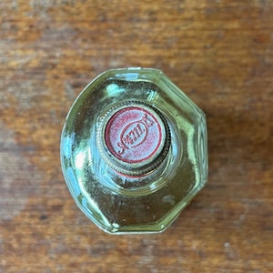 Puede incluir: Una botella de vidrio transparente con una tapa roja y dorada. La tapa tiene la palabra "JAML" impresa.