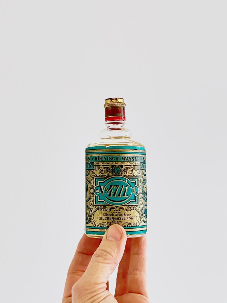 Puede incluir: Una peque&ntilde;a botella de vidrio de colonia con una etiqueta dorada y azul. La etiqueta dice "K&Ouml;LNISCH WASSER ORIGINAL EAU DE COLOGNE" y "4711". La etiqueta tambi&eacute;n incluye el texto "K&ouml;lnisch Wasser Fabrik "GLOCKENGASSE N&deg;4711" K&Ouml;LN."
