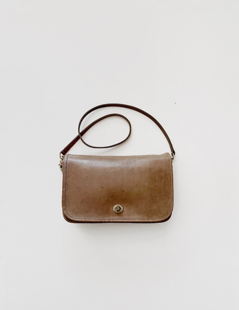 May include: A brown leather shoulder bag with a flap closure and a gold-toned clasp. The bag has a long adjustable strap.