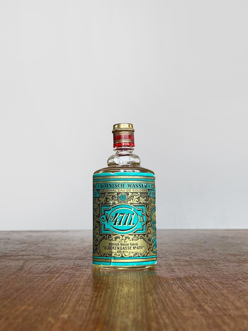 Puede incluir: Una peque&ntilde;a botella de vidrio transparente de colonia 4711. La botella tiene una etiqueta dorada con el texto "K&Ouml;LNISCH WASSER" y "GLOCKENGASSE N&deg;4711 K&Ouml;LN".