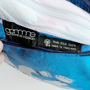 Pode incluir: Uma capa de almofada azul brilhante feita de 100% seda tailandesa. A capa possui um fecho de correr branco e duas etiquetas de tecido preto. Uma etiqueta diz "gamme dans la maison" e a outra "THAI SILK 100% MADE IN THAILAND" com um &iacute;cone de roca.