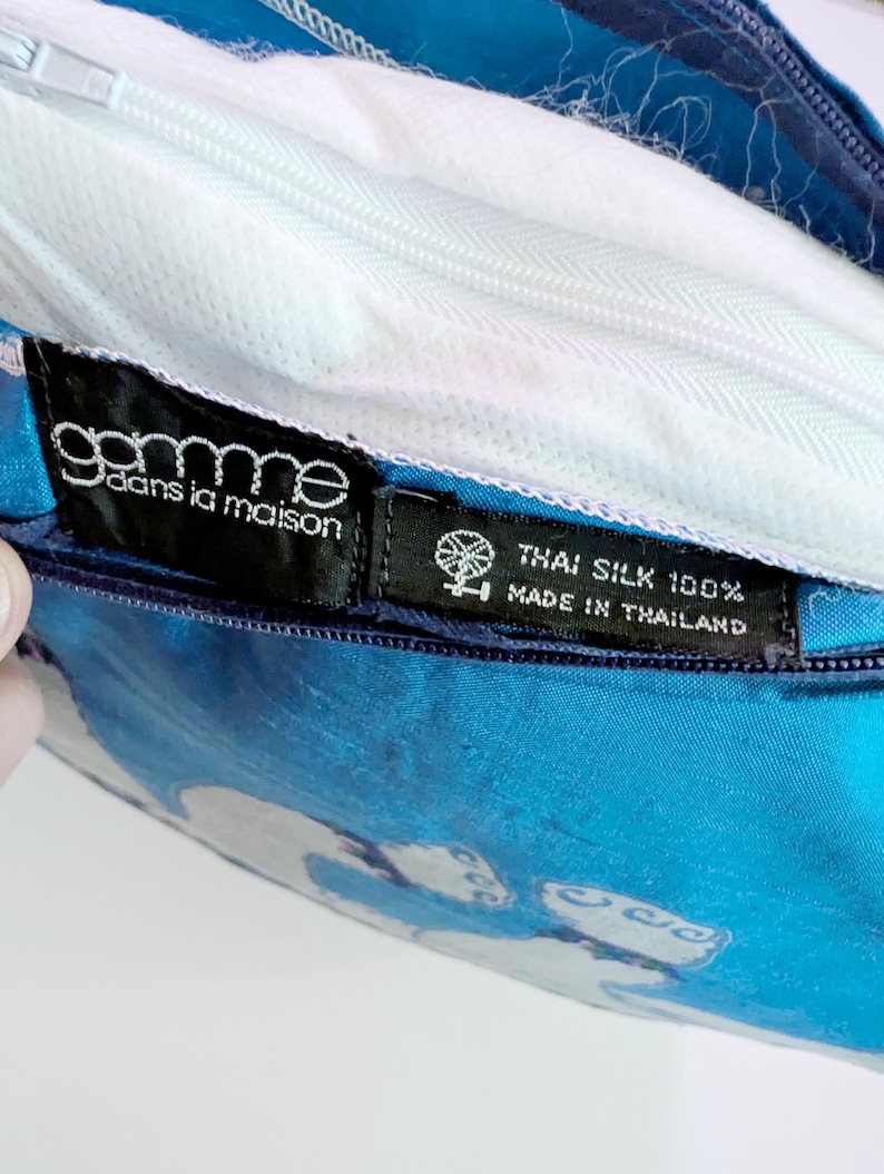 Pode incluir: Uma capa de almofada azul brilhante feita de 100% seda tailandesa. A capa possui um fecho de correr branco e duas etiquetas de tecido preto. Uma etiqueta diz "gamme dans la maison" e a outra "THAI SILK 100% MADE IN THAILAND" com um &iacute;cone de roca.