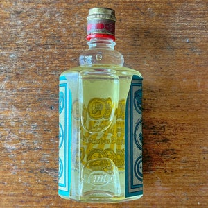 Puede incluir: Una botella de vidrio transparente con una tapa dorada y una etiqueta azul y blanca. La etiqueta tiene texto en alem&aacute;n que dice "K&ouml;lner Wasser" y "den ersten Preis".