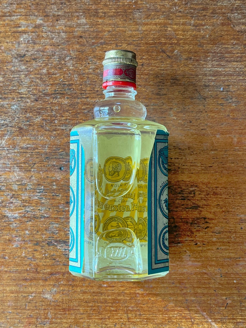 Puede incluir: Una botella de vidrio transparente con una tapa dorada y una etiqueta azul y blanca. La etiqueta tiene texto en alem&aacute;n que dice "K&ouml;lner Wasser" y "den ersten Preis".