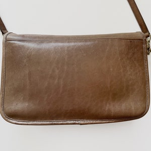 May include: A brown leather shoulder bag with a long strap. The bag has a flap closure and a gold-toned buckle.