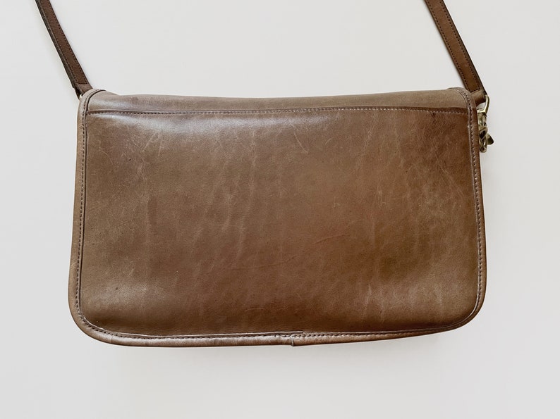 May include: A brown leather shoulder bag with a long strap. The bag has a flap closure and a gold-toned buckle.