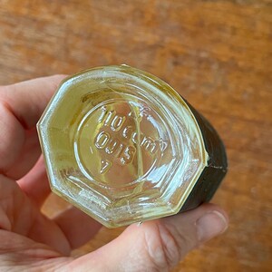 Puede incluir: Una botella de vidrio transparente con forma hexagonal y una etiqueta negra. La botella tiene una tapa de rosca y el texto "110 cc" y "Oil 15" es visible en la parte inferior de la botella.
