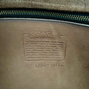 May include: Close-up of a brown leather Coach bag tag with the Coach logo and the text "THIS IS A COACH BAG, IT IS MADE OUT OF A COMPLETELY NATURAL GLOVE TANNED COWHIDE, THE SCARS, SCRATCHES, VEINS AND WRINKLES ARE NATURAL MARKINGS CHARACTERISTIC OF FULL-GRAIN LEATHERS. MADE IN NEW YORK CITY, USA. N&ordm; 094-7812"