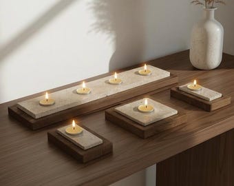 May include: A set of four candle holders featuring rectangular and square light beige stone slabs mounted on dark brown wooden bases. Each holder contains a single lit tea light candle with a small yellow flame, arranged on a wooden surface.