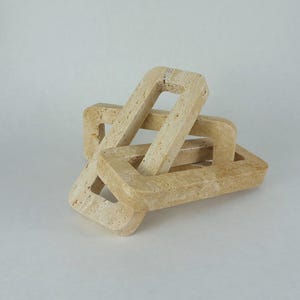 Könnte beinhalten: Eine dekorative Skulptur aus ineinandergreifenden rechteckigen Formen. Die Skulptur besteht aus einem hellbeige farbenen Steinmaterial. Die Formen sind in einem visuell interessanten, abstrakten Design angeordnet.