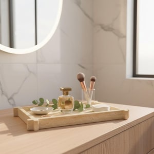 May include: A light-coloured wooden tray holds a perfume bottle, makeup brushes, a small dish with jewellery, and cotton pads. The tray is on a wooden surface, with a mirror and window in the background. The perfume bottle has a gold cap.