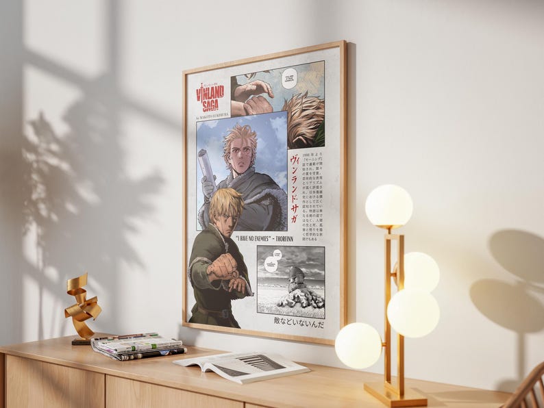 May include: A framed poster featuring artwork from the manga series "Vinland Saga." The poster has a light wood frame and displays panels of illustrations with characters and Japanese text. The color palette includes shades of blonde, green, and gray.