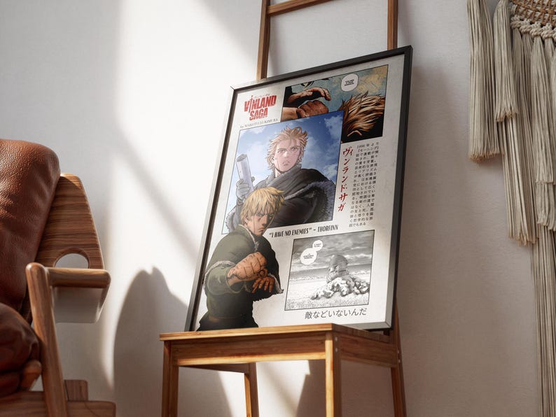 May include: Framed poster featuring artwork from "Vinland Saga" manga. The poster displays panels with characters and Japanese text. The color palette includes shades of brown, beige, and blue. The poster is propped on a wooden table.
