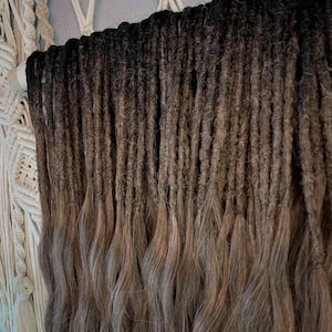 Puede incluir: Un conjunto de rastas con un degradado de color. La parte superior es negra, pasando a tonos de marrón y gris en los extremos. Las rastas son onduladas y cuelgan, creando una apariencia texturizada.