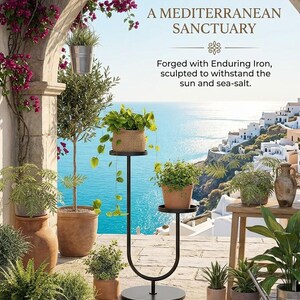 Op de afbeelding: Een zwarte metalen plantenstandaard met een U-vormige voet en twee ronde niveaus voor potplanten. De tekst luidt: A MEDITERRANEAN SANCTUARY. Forged with Enduring Iron, sculpted to withstand the sun and sea-salt. Omringd door diverse potplanten.