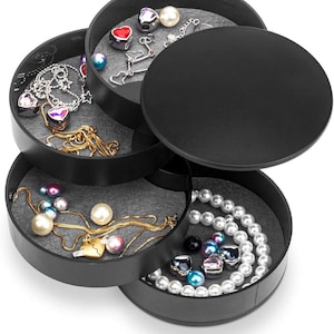 May include: A black, multi-tiered, rotating jewelry organizer with four circular compartments. Each tray features a grey felt lining and contains various necklaces, bracelets, and beads, including pearl strands and heart-shaped charms.