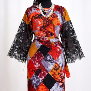 Puede incluir: Un vestido vibrante con estampado y un pañuelo y cinturón a juego. El vestido presenta un diseño de patchwork en rojo, naranja, morado y negro. Mangas de encaje negro y un collar de perlas completan el conjunto. También se ven pendientes dorados.