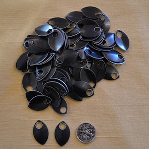 Peut inclure: Un ensemble de petites écailles métalliques noires en forme de goutte d'eau, avec un trou en haut. Les écailles sont disposées sur une surface beige, avec quelques écailles et une pièce de monnaie séparément. Idéal pour l'artisanat ou la bijouterie.