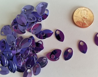 May include: A pile of purple metallic leaf-shaped charms with a hole for stringing. The charms are about the size of a US penny.