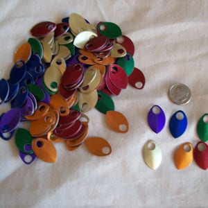 May include: A pile of colorful metal scales in various shades of red, orange, yellow, green, blue, and purple. The scales are arranged in a loose pile, with some of the scales overlapping. There are also a few individual scales arranged in a row below the pile.