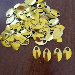 May include: A large pile of gold-colored metal scales with a hole in each one. There are five individual scales in a row below the pile.