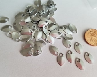 May include: A pile of silver metal scales with a hole in the center of each scale. The scales are about the size of a US penny.