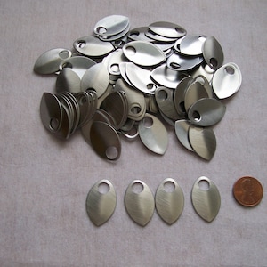 May include: A pile of silver metal leaf-shaped charms with a hole in the top. The charms are about the size of a US penny.