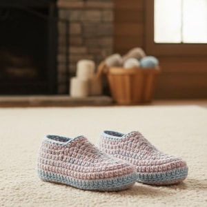 May include: A pair of handmade crochet slippers in soft pastel colors. The slippers feature a light pink and blue color scheme, with a textured stitch pattern. The slippers are designed for indoor wear and are placed on a neutral-colored rug.