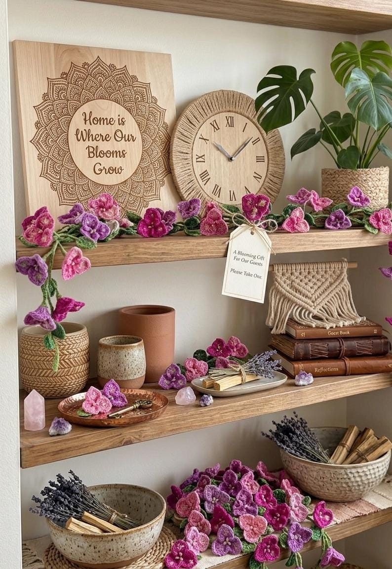 May include: Wooden shelves display home decor items, including a wooden sign with the text "Home is Where Our Blooms Grow", a woven clock, and crochet flowers. Other items include books, a plant, and a bowl of lavender.
