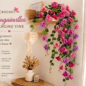 May include: Crochet bougainvillea hanging vine in shades of pink and purple. The handmade floral arrangement includes green leaves and is displayed on a wooden shelf. The text reads "Bring nature's beauty into your home."