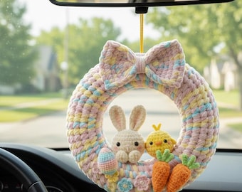 May include: A pastel-colored crochet Easter wreath with a bow at the top, hanging from a car's rearview mirror. The wreath features a bunny, chick, carrots, and an Easter egg. The wreath is approximately 8 inches in diameter.