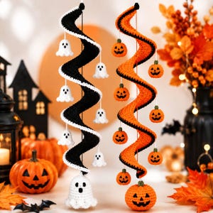May include: Two hanging spiral decorations made of crocheted yarn. One spiral is black with white crocheted ghost figures attached, and the other is orange with small crocheted jack-o'-lantern pumpkins attached, each featuring green stems.