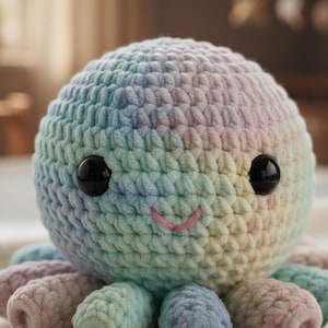 May include: A crocheted octopus in pastel rainbow colors. The plush toy has a round head with large black eyes and a smiling pink mouth. The tentacles are in shades of blue, pink, and purple.
