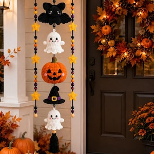 May include: A hanging mobile featuring crocheted Halloween figures including a black bat, two white ghosts, an orange jack-o'-lantern, and a black witch hat. The figures are strung with black, orange, and purple beads and yellow stars.