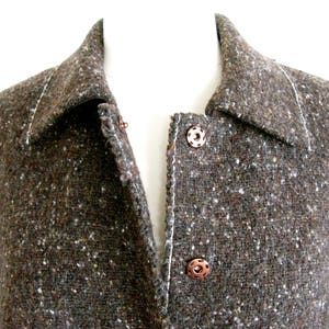 May include: A brown tweed jacket with a collar and two buttons. The jacket has a speckled pattern and a white stitching detail.