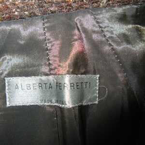 May include: A close-up of a brown wool jacket with a black satin lining. The label reads "Alberta Ferretti! Made in Italy."